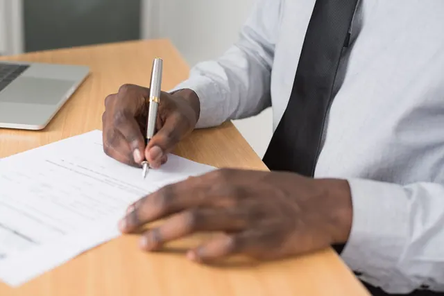 Close-up of a man signing paperwork on a desk, with a laptop nearby, in a professional office environment. Corporation formation guide: what to know and why