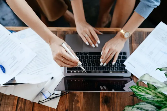 Top view of anonymous women browsing modern netbook while sitting at wooden desk with stack and documents during work in office. Entity type selection examples compared: what the good ones share