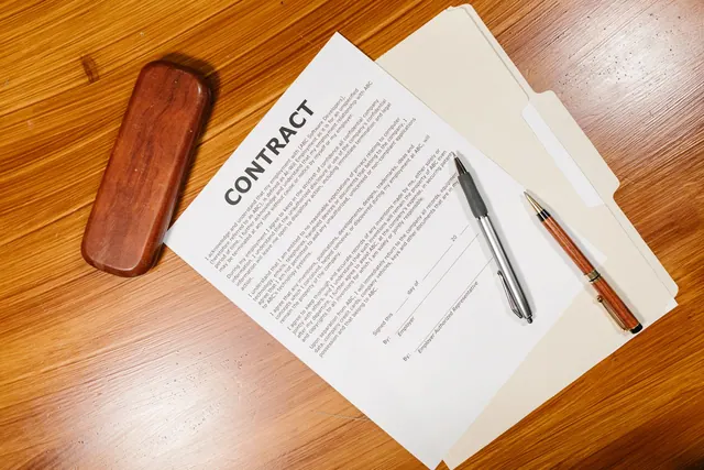 High-angle view of a contract document with pens and a case on a wooden table. Sole proprietorships examples: what the cases show